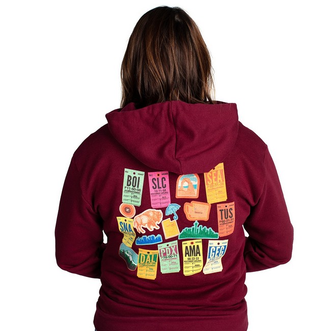Back of a maroon hoodie with a colorful collage of retro luggage tags and airport codes